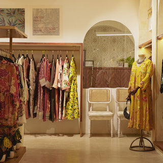 A boutique displaying vibrant kurta sets on hangers, with a mannequin in a yellow gown and two elegant chairs in the background.