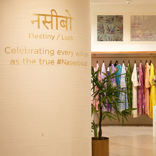 Interior of a boutique showcasing colorful garments, with a focus on a wall displaying the phrases "Destiny/Luck" and celebrating women.